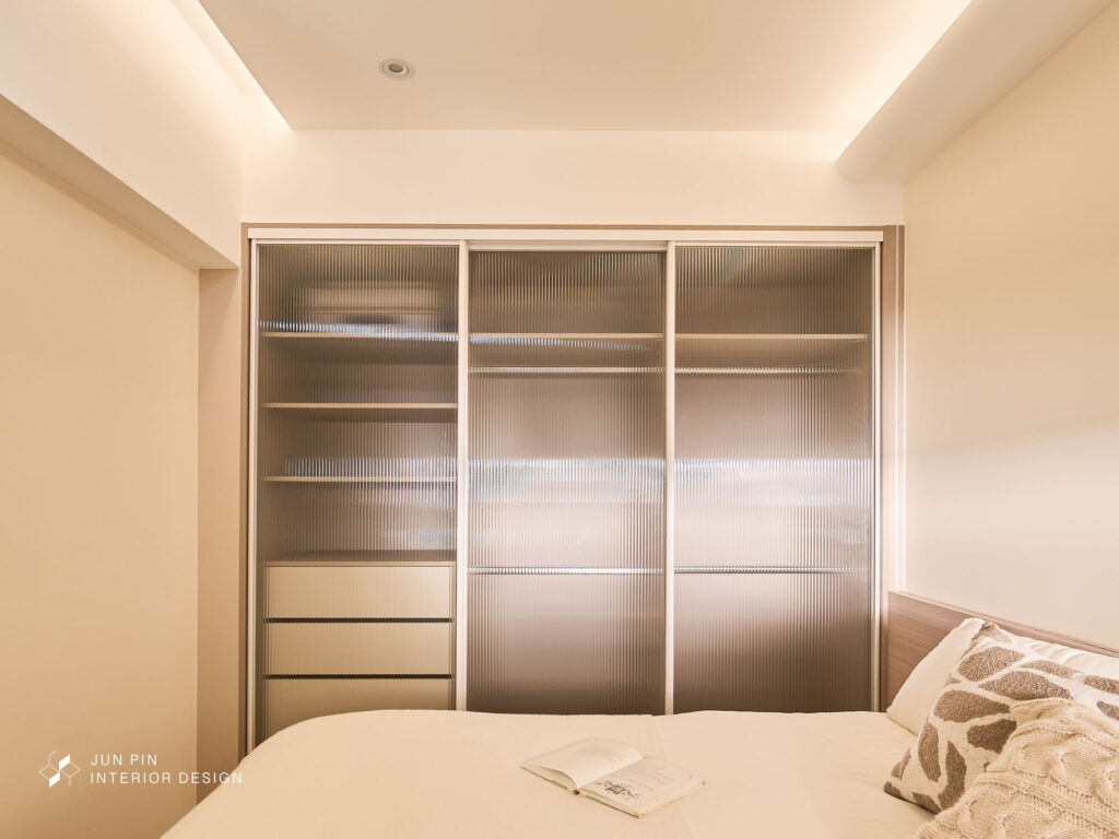 主臥以隱藏門連接客廳，延續整體立面整潔感。 床頭背板使用淺木飾面，搭配鋁條燈光帶，營造出柔和的光影氛圍。