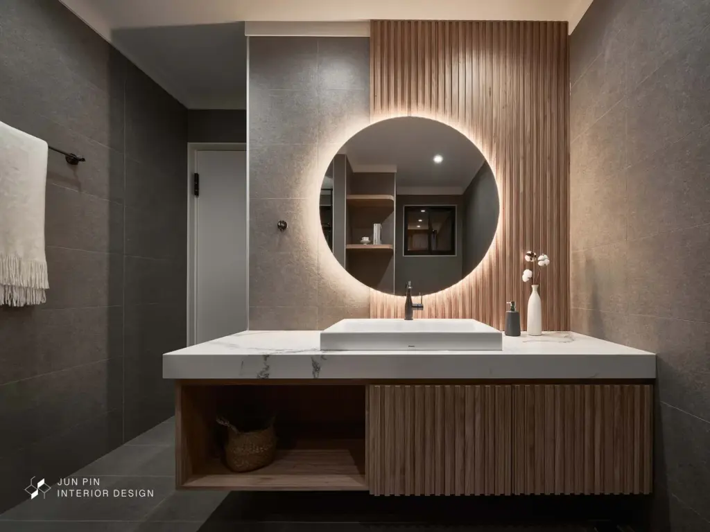 客浴室則以沉穩灰調呈現，搭配木紋地磚與圓鏡背光，結合格柵元素，營造如飯店般的精緻質感。