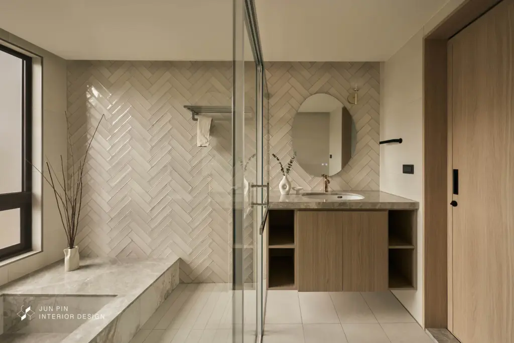 主浴空間則以降板式浴缸作為視覺與使用重點，浴缸與面盆檯面皆採用大理石鋪設，壁面以人字拼方式呈現，提升細節層次。