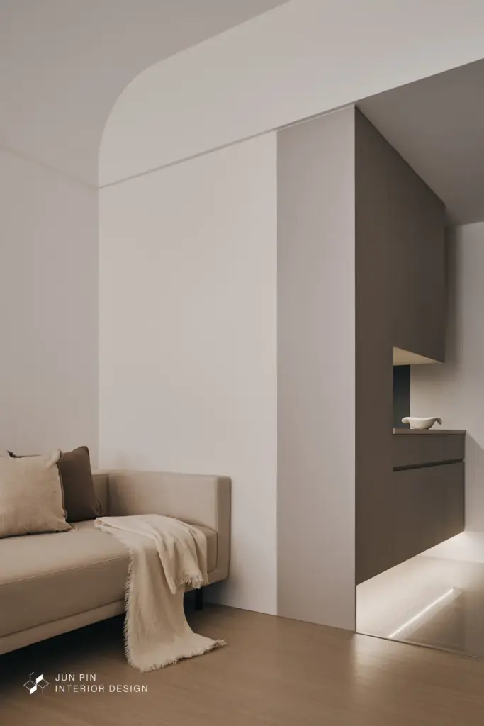 考量玄關本身尺度不大，設計上並未將櫃體全數做滿，而是透過局部留白、底部懸空與燈光安排，減輕入門時的壓迫感，也讓櫃體視覺更顯輕盈。鏡面則以灰鏡形式融入立面，不僅放大空間感，也延續整體溫潤低彩度的設計調性。