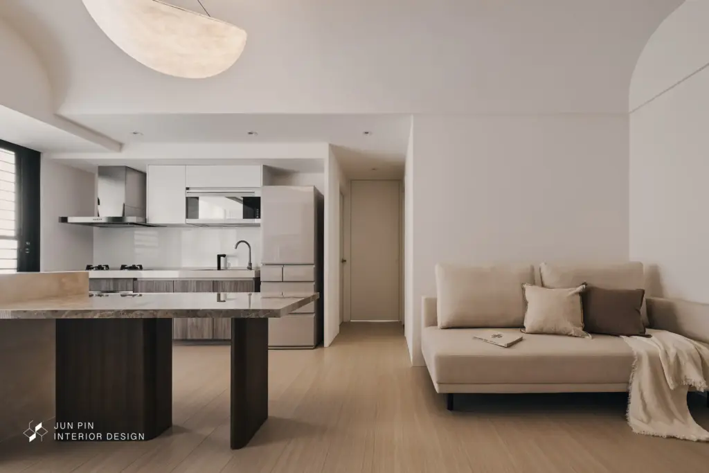 公領域依照屋主實際生活習慣重新配置，將原本客廳與餐廳位置對調，把採光更好的區域留給中島與餐桌，放大聚會、交流與共享日常的可能；客廳則以藝術展示感為概念，透過退縮牆面、弧形收邊與霧面特殊塗料，弱化電視存在感，讓空間更像一面靜靜展出的畫牆。