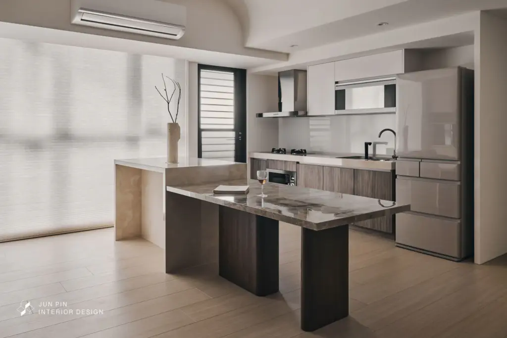 中島除了延伸料理與備餐機能，也結合紅酒櫃規劃，回應屋主對收藏與招待朋友的生活想像。檯面選用紋理柔和、色調溫潤的材質，與整體奶茶、白與暖咖色系相互呼應，營造出舒適且具有質感的共享場域。中島與餐桌的搭配，也讓餐廚空間在日常與聚會之間保有更高的彈性。