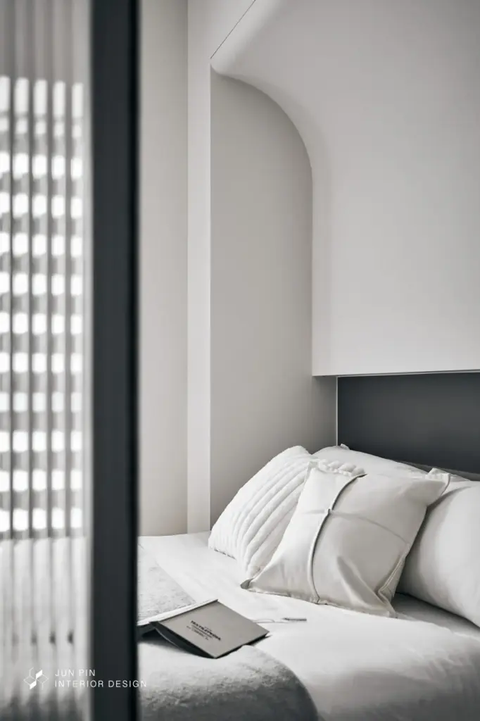 在不更動格局的前提下，以大圓弧造型包覆床頭上方的結構樑，完美化解樑壓床的疑慮並柔化空間線條。進門處規劃跳色開放式衣櫃，並在衛浴前運用灰玻門片放大更衣區視感，營造出靜謐且具備飯店質感的睡眠環境。