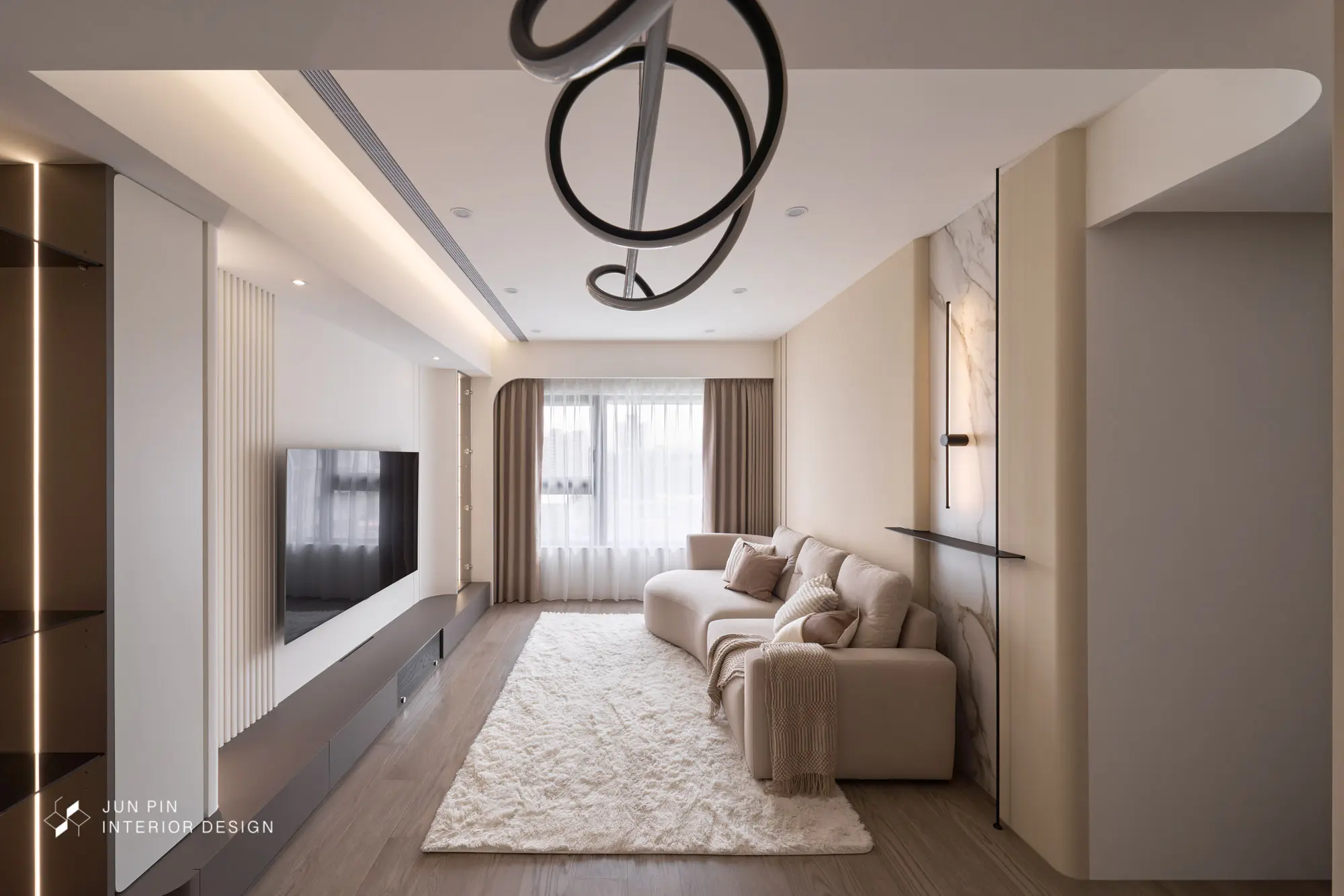 郡品室內設計現代輕奢新成屋案例現代輕奢風客廳全景，圓弧造型電視牆結合格柵與灰色電視櫃，米色曲線沙發、線條造型吊燈與大面窗簾。